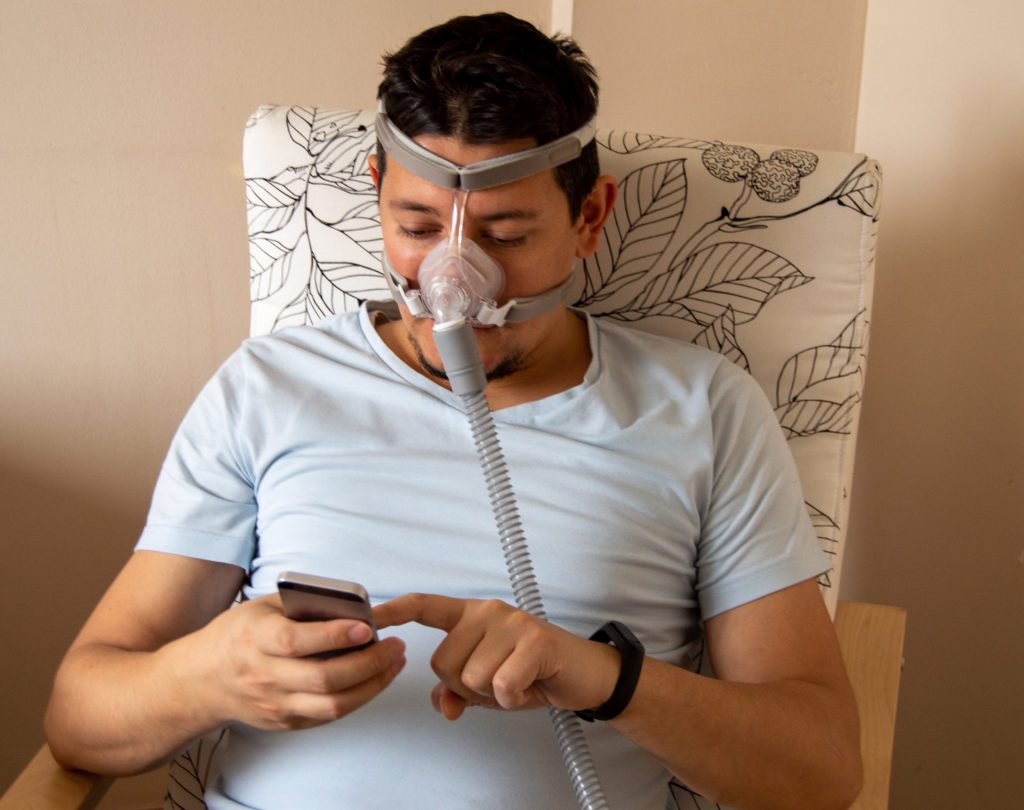 Man getting used to his CPAP mask while on his cellphone